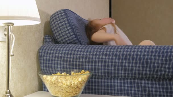 Une petite fille est assise sur le canapé à regarder la télévision et à manger du pop-corn
 - Séquence, vidéo