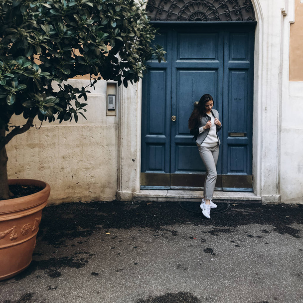 Вид молодой женщины с длинными волосами, позирующей у синей двери старинного здания
 - Фото, изображение