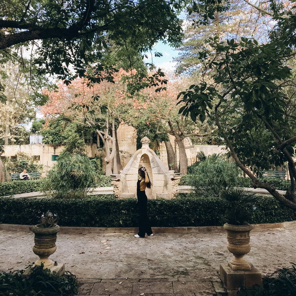 Nainen yllään musta romper, keltainen hyppääjä ja valkoinen lenkkarit kävely vanhassa puutarhassa
. - Valokuva, kuva