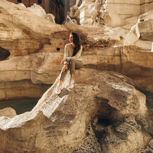 古代の噴水の近くの岩に長い髪のポーズを持つ若い女性のビュー - 写真・画像