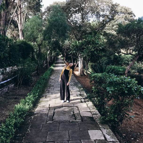 Frau mit schwarzem Strampler, gelbem Pullover und weißen Turnschuhen läuft auf Gasse im alten Garten. - Foto, Bild