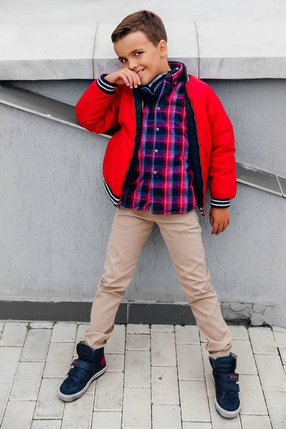 Fashion kid fall time in the city stands against the background of a concrete wall. - Foto, Imagen