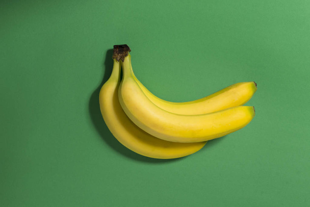 緑の背景にバナナが 3 本. - 写真・画像