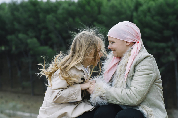 Μια γυναίκα με καρκίνο είναι δίπλα στην κόρη της. Αγκαλιάζει μια κοπέλα  - Φωτογραφία, εικόνα