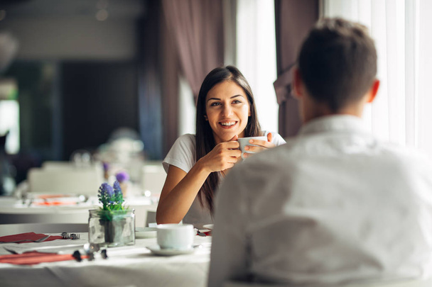 Smiling woman on a date in a restaurant,having a conversation over a meal in hotel.Cheerful female customer drinking coffee with a partner.Positive emotions,love,affection.Public place behave manners - Foto, imagen