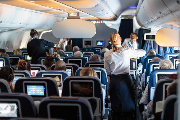 Інтер'єр великого комерційного літака зі стюардесами, що обслуговують пасажирів на місцях під час польоту
. - Фото, зображення