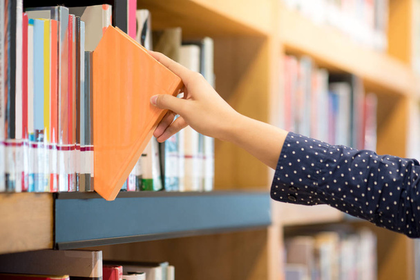 αρσενική χέρι picking πορτοκαλί βιβλίο στη βιβλιοθήκη - Φωτογραφία, εικόνα