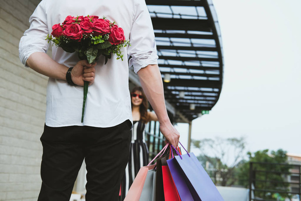 homem segurando saco de compras & buquê de rosas vermelhas atrás de suas costas
  - Foto, Imagem