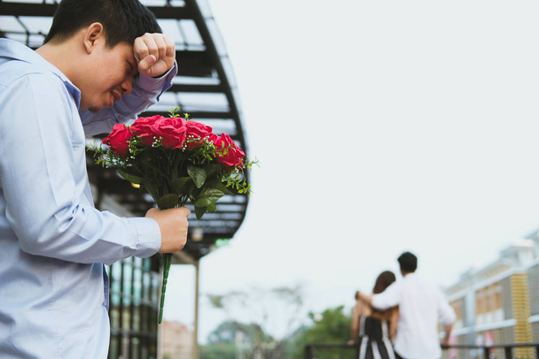 Сердобольный мужчина, держа в руках букет красных роз, грустит, пока
 - Фото, изображение