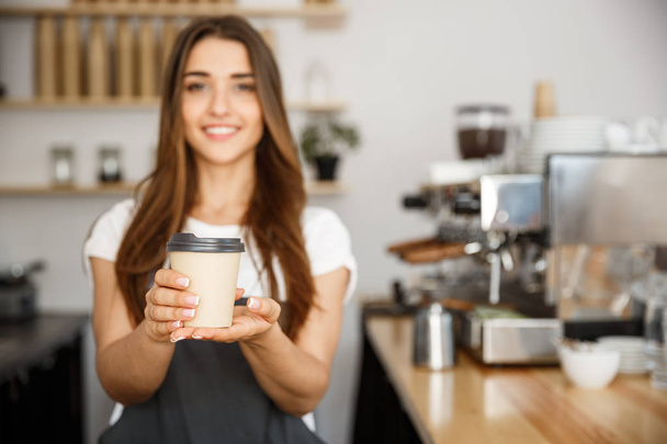 Coffee Business Concept - Beautiful Caucasian lady smiling at camera offers disposable take away hot coffee at the modern coffee shop - Photo, Image