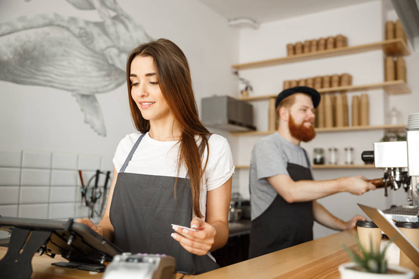 Káva obchodní koncept - krásné ženské barista poskytování platebních služeb pro odběratele s kreditní kartou a usmíval se při práci v baru čítačů v moderní kavárně. - Fotografie, Obrázek