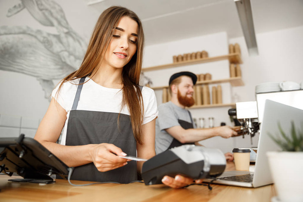 Kaffee-Business-Konzept - schöne weibliche Barista gibt Zahlungsservice für Kunden mit Kreditkarte und lächelt, während sie an der Theke in einem modernen Café arbeitet. - Foto, Bild