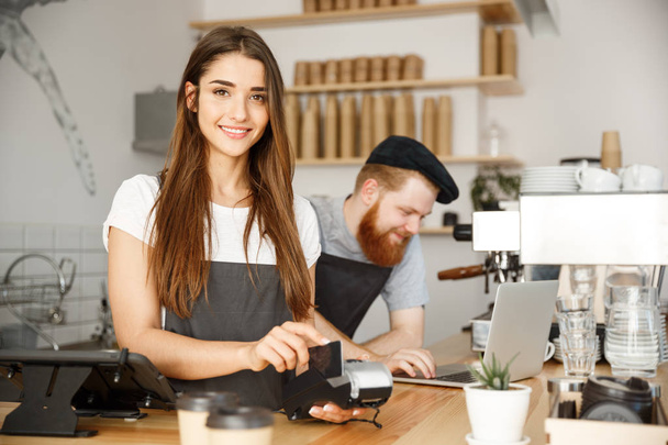 Coffee Business Concept - Belle femme barista donnant un service de paiement pour le client avec carte de crédit et souriant tout en travaillant au comptoir du bar dans le café moderne
. - Photo, image