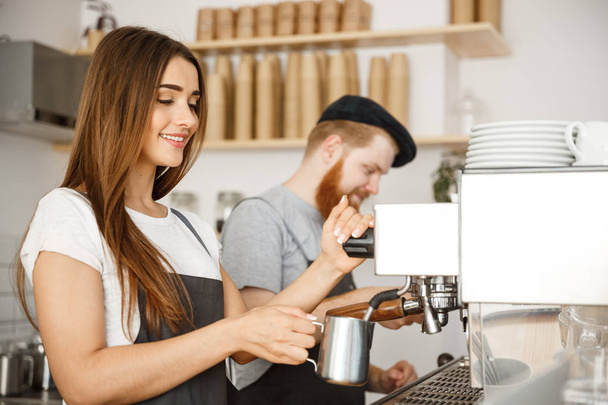 Coffee Business Concept - retrato de la señora barista en delantal preparando y humeante leche para el pedido de café con su pareja mientras está de pie en la cafetería
. - Foto, Imagen