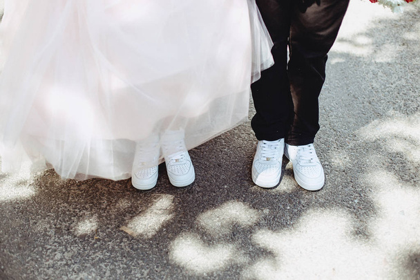 Beine der Braut auf dem Bürgersteig in Turnschuhen und Kleidern - Foto, Bild