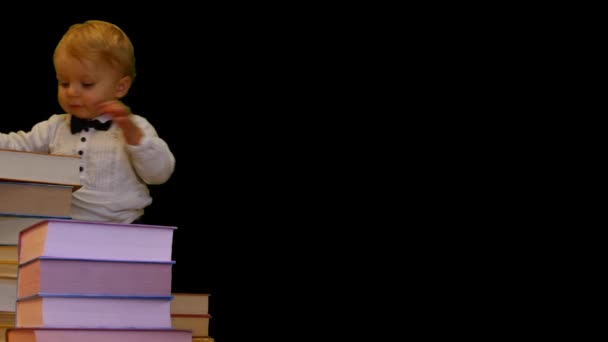 cute 1 year baby supports on pile of books on black background - Footage, Video