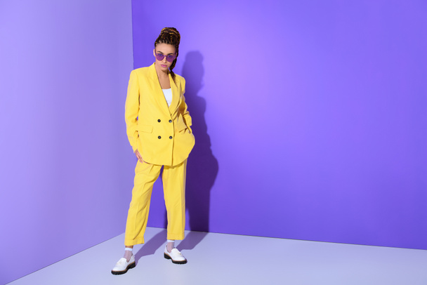 african american girl posing in trendy yellow suit and purple sunglasses, on ultra violet background - Foto, Imagem