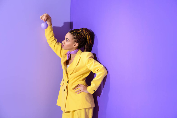 african american girl posing in yellow suit with purple apple, on trendy ultra violet background - Φωτογραφία, εικόνα