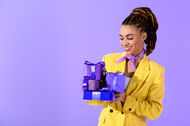 african american girl in yellow suit holding purple  presents, on trendy ultra violet background - 写真・画像