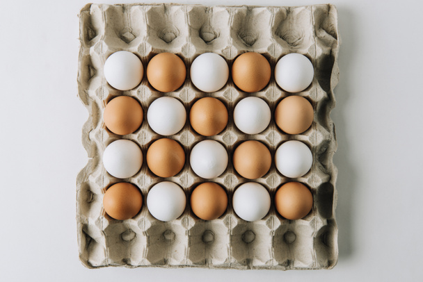white and brown eggs laying in egg carton on white background - 写真・画像