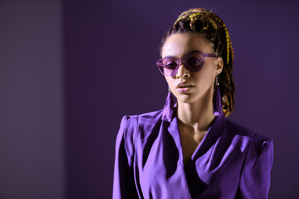 fashionable african american girl posing in trendy ultra violet jacket and sunglasses - 写真・画像