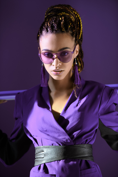 Stylish mulatto girl posing in ultra violet jacket and sunglasses, isolated on purple - Fotoğraf, Görsel