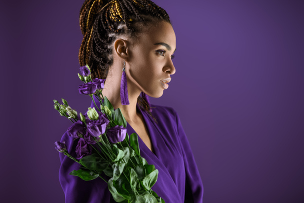 Fashionable african american girl posing with purple eustoma flowers, isolated on purple, ultra violet trend - Fotó, kép