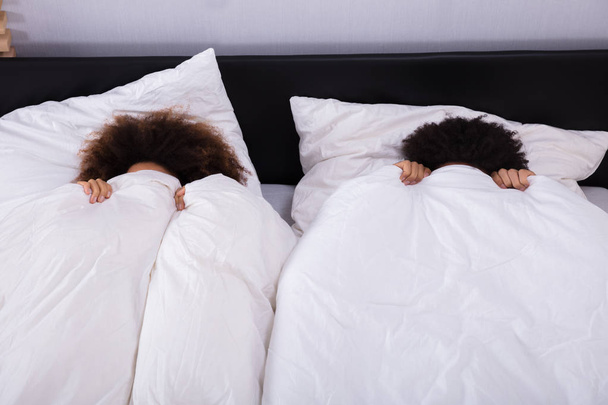 Elevated View Of Couple Covering Their Face With White Sheet In Bedroom - Foto, afbeelding