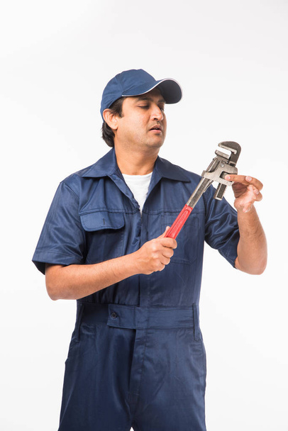 Indian plumber in action with Pipe wrench or plumbing spanner, standing isolated over white background - Photo, Image