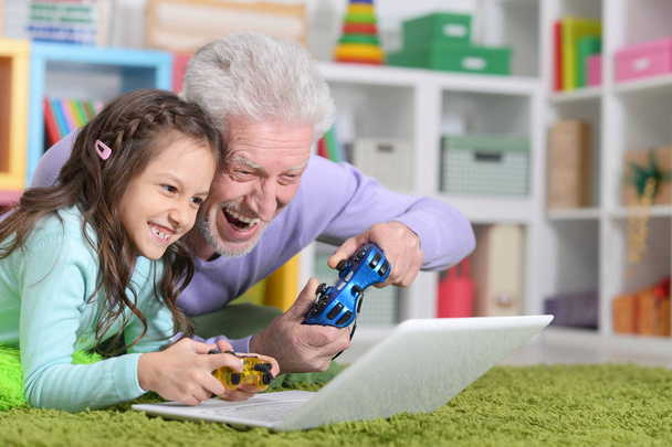 Emotional senior man with granddaughter playing computer game on laptop at home - Foto, Imagem