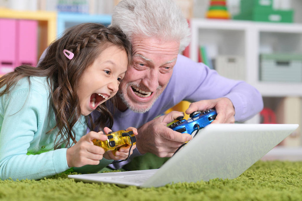 Emotional senior man with granddaughter playing computer game on laptop at home - Photo, image