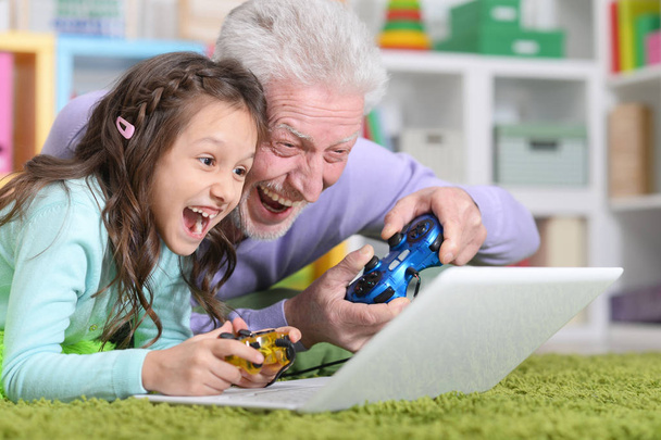 Emotional senior man with granddaughter playing computer game on laptop at home - Φωτογραφία, εικόνα
