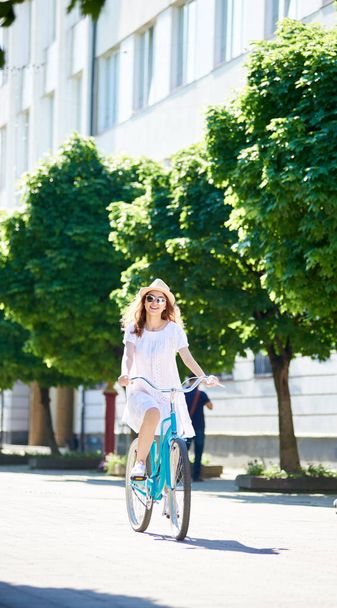 Eine junge Frau auf einem blauen Fahrrad fährt allein die Stadtstraße hinunter.  - Foto, Bild