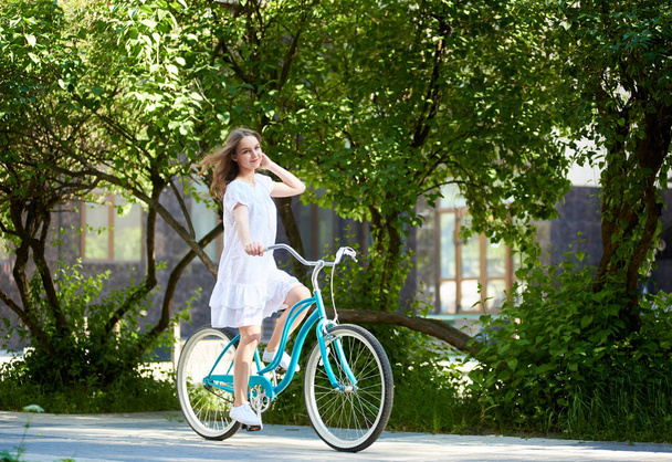 Giovane donna dai capelli lunghi in un vestito in bicicletta nel parco
 - Foto, immagini