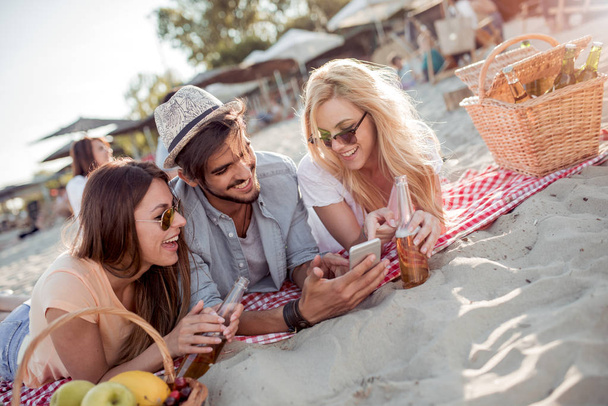 ein Mann und zwei Frauen liegen am Strand, trinken Bier und reden - Foto, Bild