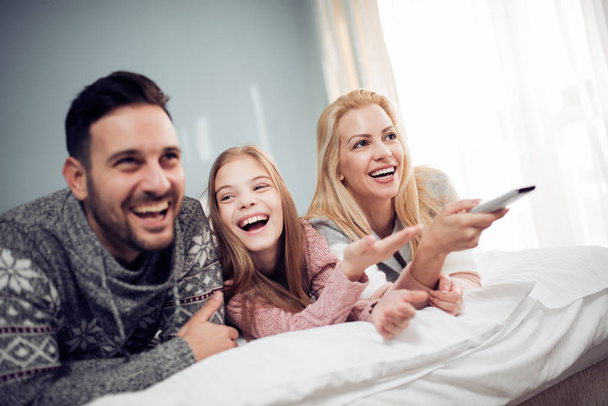Familia viendo la televisión en el dormitorio y riendo
  - Foto, Imagen