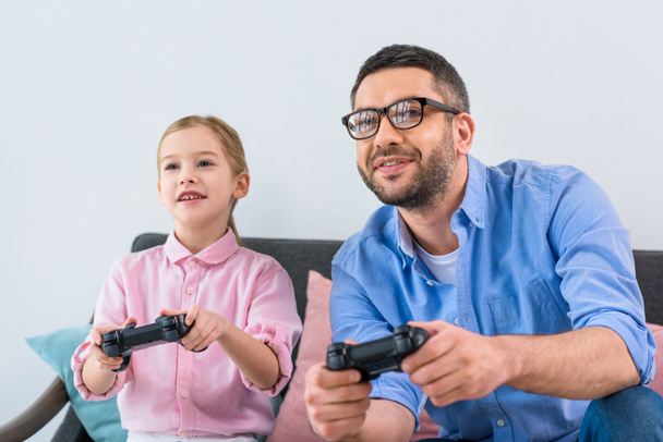 Portret van dochter en vader afspelen van video game samen thuis - Foto, afbeelding