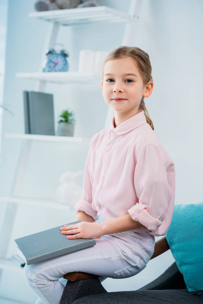 portrait of adorable little kid with book sitting on sofa at home - Foto, Bild
