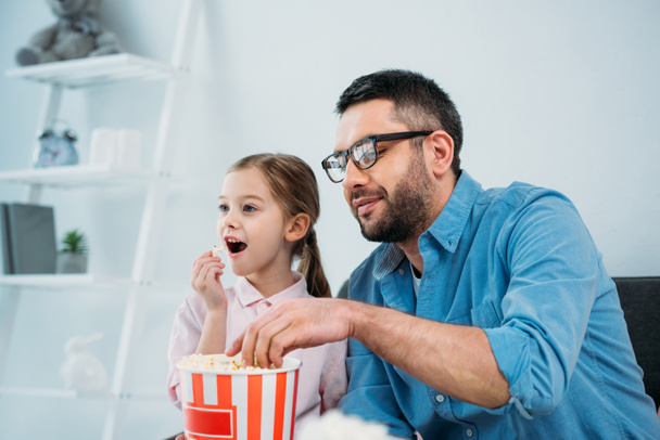 батько і дочка їдять попкорн під час перегляду телевізора вдома
 - Фото, зображення