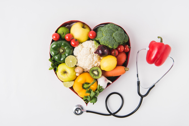 verduras y frutas que ponen en plato en forma de corazón cerca de pimienta con estetoscopio aislado sobre fondo blanco
     - Foto, Imagen