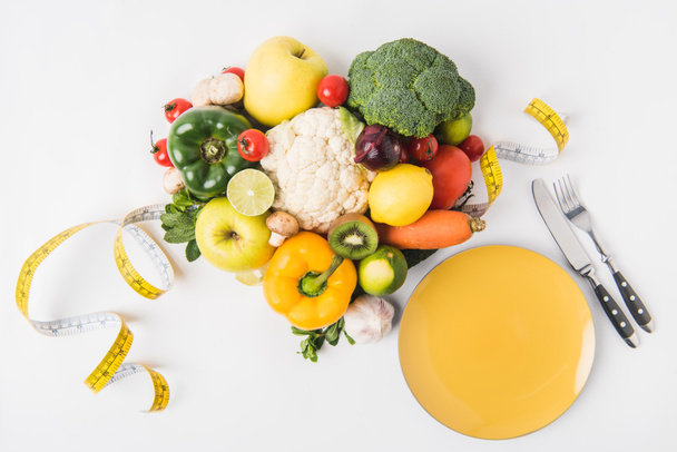 vegetables and fruits laying on white background with fork, spoon, measuring tape and plate - Photo, Image