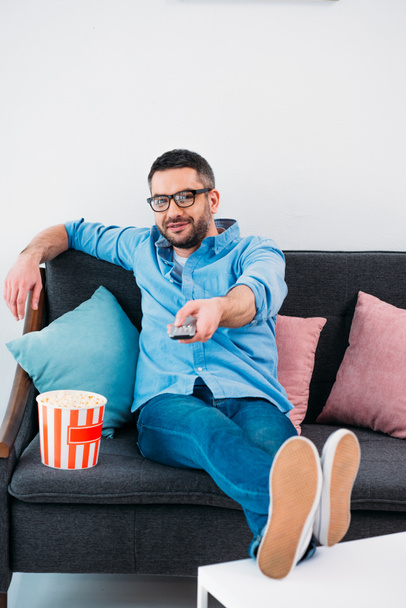 man in eyeglasses resting on sofa and watching tv at home - Foto, Imagen