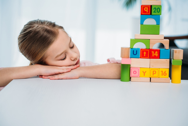 child sleeping on table with pyramid made of colorful blocks - Photo, Image