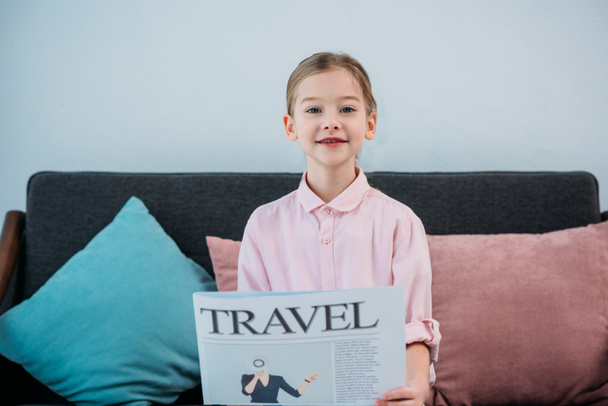 portrait of cute child with travel newspaper in hands sitting on sofa - Photo, Image