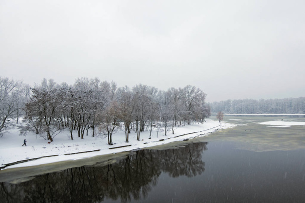 Winter landscape of the Dnipro River and park at the bank. Snow covers tree's brunches and ground. Kyiv, Ukraine - Photo, Image