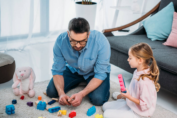 little daughter and father playing with colorful blocks together on floor at home - Photo, Image
