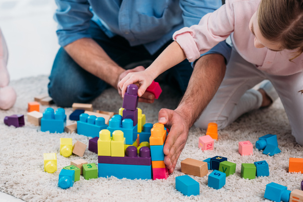 cropped shot of daughter and father playing with colorful blocks together on floor at home - Fotó, kép