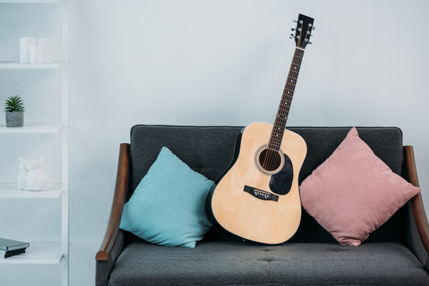 vista de cerca de la guitarra acústica en el sofá con almohadas en la sala de estar
 - Foto, Imagen