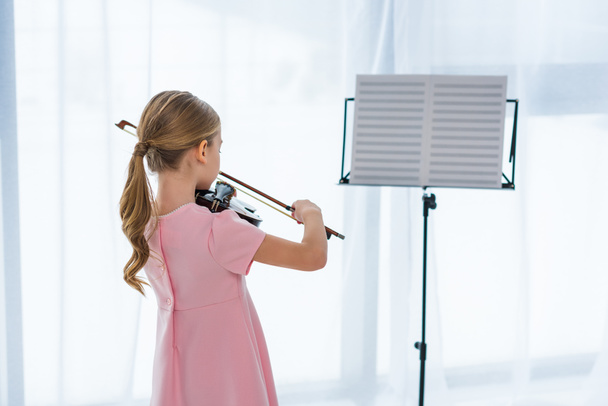vista posteriore del bambino in abito rosa che suona il violino a casa
 - Foto, immagini