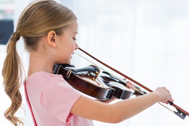 自宅でバイオリンを弾いてピンクのドレスかわいい小さな子供の側面図 - 写真・画像